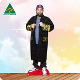 Cardboard cutout of a person wearing a black coat with gold accents and a purple cap, on a wooden floor with a colorful gradient background.